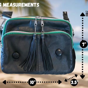 Puede incluir: Bolso de cuero negro con ribete verde y cremalleras plateadas. El bolso tiene dos borlas negras y dos botones negros redondos. El bolso mide 25,4 cm de ancho, 17,8 cm de alto y 8,9 cm de profundidad. El texto "BAG MEASUREMENTS" est&aacute; en la parte superior.