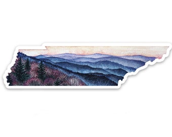 May include: A sticker in the shape of the state of Tennessee, featuring a watercolor painting of a mountain landscape. The artwork depicts layers of blue and purple mountains under a pink and orange sky, with trees in the foreground.