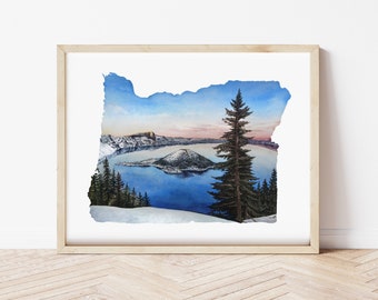 Puede incluir: Pintura a la acuarela del Crater Lake en Oregón, enmarcada en madera clara. La obra representa las aguas azules del lago, una isla central y montañas nevadas bajo un cielo azul y rosa, con árboles de hoja perenne en primer plano.