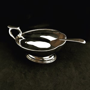 Puede incluir: Un plato de servir de plata con un asa y una cuchara a juego. El plato tiene un borde festoneado y un borde con cuentas.