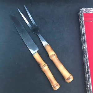 Peut inclure: Un ensemble de deux ustensiles de cuisine avec des manches en bambou. Les ustensiles sont un couteau et une fourchette. Le couteau a une lame dentelée et la fourchette a trois dents.