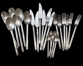 May include: A collection of stainless steel flatware featuring five large spoons, four dinner knives, five dinner forks, and five small teaspoons. Each piece has a brushed matte finish with simple, straight handles and rounded edges.