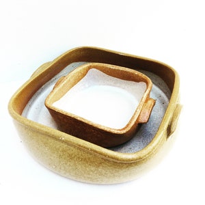Könnte beinhalten: Ein Set aus zwei Keramik-Backformen. Die größere Form ist quadratisch mit abgerundeten Kanten und einer hellbraunen Glasur. Die kleinere Form ist quadratisch mit abgerundeten Kanten und einer dunkelbraunen Glasur. Beide Formen haben ein weißes Innenleben.