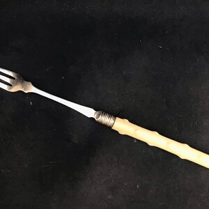 Pode incluir: Um garfo de prata com cabo de osso branco. O garfo tem um design tradicional com três dentes.