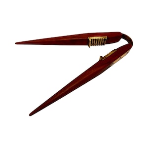 以下が含まれることがあります： 真鍮の蝶番とギザギザの縁が付いた木製のナッツクラッカー。ナッツクラッカーは閉じており、赤褐色をしています。