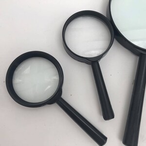K&ouml;nnte beinhalten: Drei schwarze Handlupen in verschiedenen Gr&ouml;&szlig;en. Die Lupen haben schwarze Kunststoffgriffe und klare Glaslinsen.
