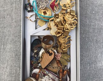 May include: A silver box filled with a variety of jewellery, including necklaces, bracelets, rings, and charms. The jewellery is made of gold, silver, and other materials. There are also some wooden and beaded items in the box.