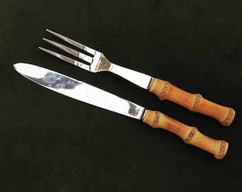 May include: A set of two silver utensils with bamboo handles. The fork and knife have a polished silver finish and are designed with a simple, elegant style.