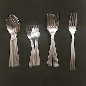 Può includere: Un set di posate, tra cui cucchiai e forchette, con finitura argentata e design rigato. Le posate sono disposte in tre gruppi su uno sfondo nero.