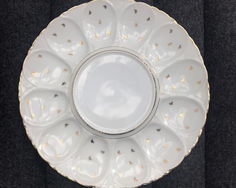 May include: A white porcelain serving dish with a gold rim and a central serving area surrounded by 12 individual serving sections. The dish is decorated with a repeating pattern of small gold fleur-de-lis.