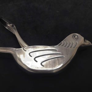 May include: Silver bird-shaped citrus juicer with a lever handle. The juicer has a textured design on the body.