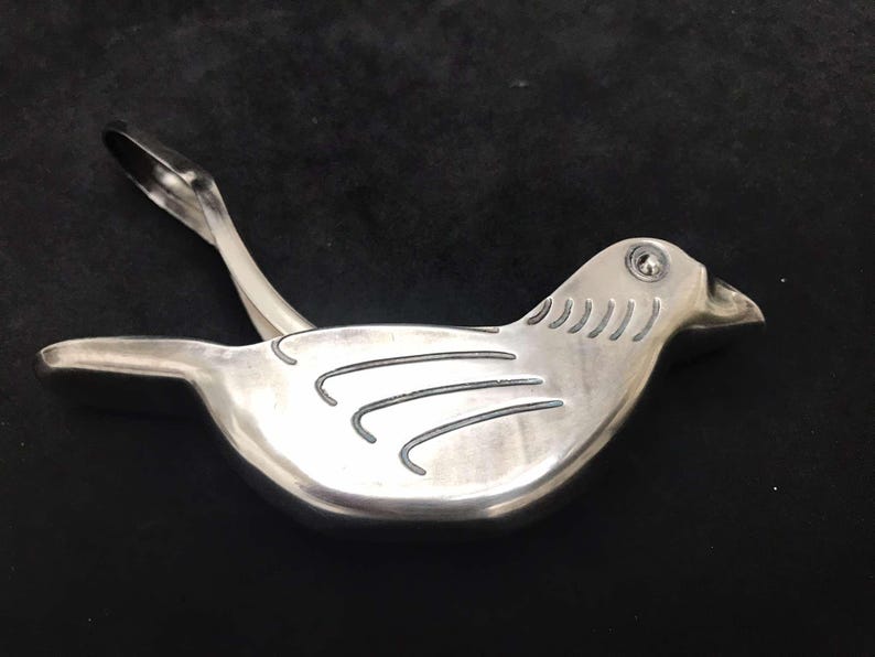 May include: A silver bird-shaped citrus juicer with a lever on the back. The bird has a detailed design on its wings and a small hole in its beak.
