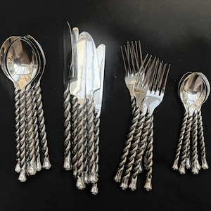 May include: A set of silver-colored flatware with a unique twisted rope design on the handles. The set includes spoons, knives, and forks, all arranged on a dark surface. The spoons, knives, and forks have a shiny, reflective finish.
