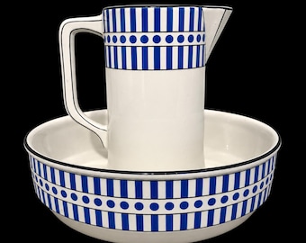 Op de afbeelding: Een witte keramische kan en bijpassende waskom met een patroon van blauwe verticale strepen en een horizontale band met blauwe stippen. Beide stukken hebben een witte binnenkant en een dunne zwarte rand langs de bovenkant.