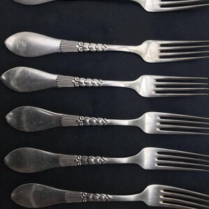 May include: Five vintage silver forks with ornate handles. The handles have a detailed design with vertical lines and a series of small, connected circles. The tines of the forks are visible, and the silverware is arranged against a dark background.