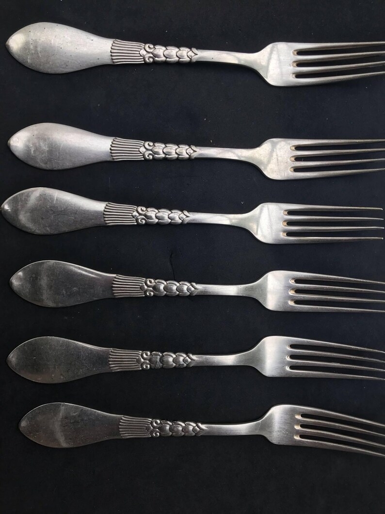 May include: Five vintage silver forks with ornate handles. The handles have a detailed design with vertical lines and a series of small, connected circles. The tines of the forks are visible, and the silverware is arranged against a dark background.