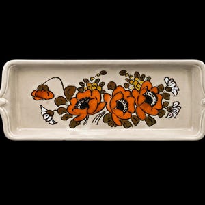 Könnte beinhalten: Ein rechteckiges Serviertablett aus Keramik mit cremefarbener Basis und einem zentralen, handgemalten Blumenmotiv. Das Design zeigt drei große, leuchtend orangefarbene Mohnblumen mit dunkelbraunen Mitten, umgeben von kleinen weißen Blüten.