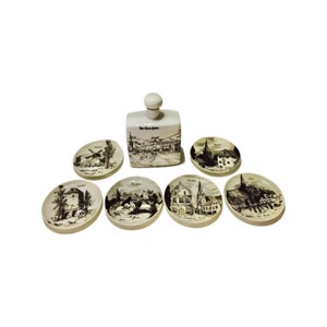 Può includere: Set di sei sottobicchieri in ceramica bianca con illustrazioni in bianco e nero di diversi edifici. I sottobicchieri sono progettati per abbinarsi a una bottiglia in ceramica bianca con un'illustrazione in bianco e nero di una città.
