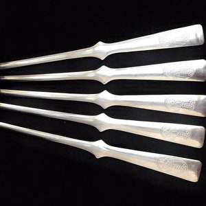 Peut inclure: Six ouvre-lettres argentés sur fond noir. Chaque ouvre-lettre a une longue lame fine et un manche rectangulaire avec un motif en relief. Les ouvre-lettres sont légèrement inclinés, créant une sensation de profondeur.