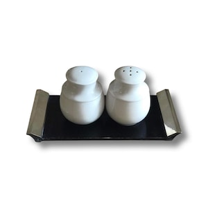May include: A set of two white ceramic salt and pepper shakers on a black tray with silver accents.