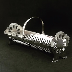 May include: A silver, decorative serving tray with a handle. The tray has a delicate, openwork design and is perfect for serving bread or other small items.