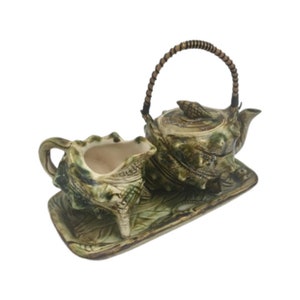 Peut inclure: Un service à thé en céramique avec une théière, un pot à crème et un plateau. L'ensemble est décoré d'un glaçage vert et brun et présente un motif de coquille.