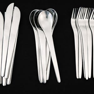 Könnte beinhalten: Ein Set aus Edelstahlbesteck, darunter Messer, Löffel und Gabeln, vor einem schwarzen Hintergrund angeordnet. Das Besteck hat eine polierte, reflektierende Oberfläche, die eine elegante und moderne Ästhetik erzeugt. Die Anordnung hebt die verschiedenen Utensilien hervor.