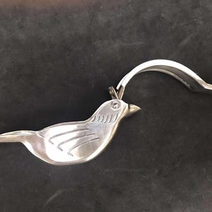 May include: A silver bird-shaped garlic press with a hinged lever. The press is open, showing the interior.