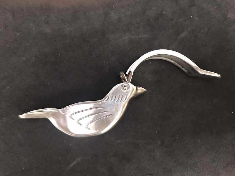 May include: A silver bird-shaped garlic press with a hinged lever. The press is open, showing the interior.
