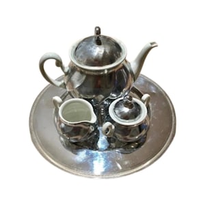 Puede incluir: Un juego de té de plata con una tetera, una jarra de crema y un azucarero en una bandeja de plata. El juego está hecho de porcelana con un acabado plateado.