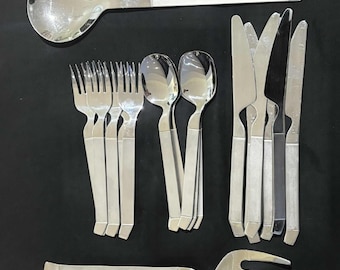 May include: A collection of polished silver flatware, including forks, spoons, knives, and a serving spoon. The utensils have a simple, modern design with rectangular handles. The arrangement suggests a formal dining setting.