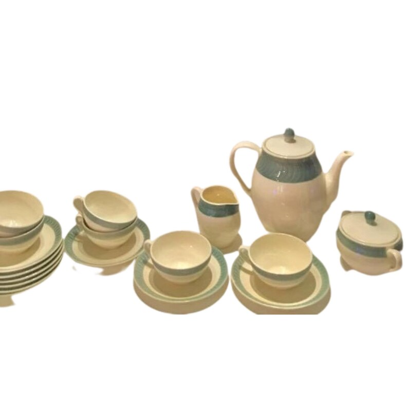 May include: A ceramic tea set featuring a cream-colored base with a muted teal band pattern. The set includes a teapot with a lid, a creamer, a sugar bowl with a lid, four teacups with matching saucers, and a stack of additional saucers.