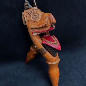 Op de afbeelding: Een houten notenkraker gesneden in de vorm van een mythisch wezen met een rood geverfde mond en tong. Het wezen heeft een groot, rond oog en een hoorn op zijn hoofd.