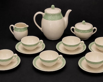 Peut inclure: Un service à thé composé d'une théière, d'un pot à lait, d'un sucrier avec couvercle et de six tasses avec soucoupes assorties. Chaque pièce est blanc cassé avec une bande décorative vert pâle ornée d'un motif tourbillonnant répétitif.