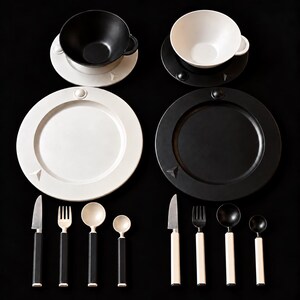 May include: A dinnerware set featuring two bowls, two plates, and eight utensils. One bowl is black on a white saucer, the other is white on a black saucer. The plates match their respective saucers. Utensils have contrasting black and white handles.