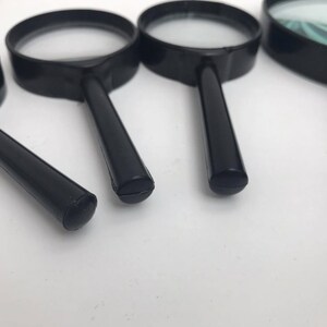 K&ouml;nnte beinhalten: Vier schwarze Handlupen mit klaren Linsen. Die Lupen sind in verschiedenen Gr&ouml;&szlig;en und in einer Reihe auf einer wei&szlig;en Oberfl&auml;che angeordnet.