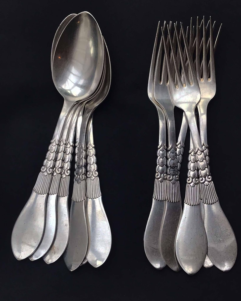 May include: A collection of silver-colored spoons and forks arranged against a black background. The spoons have a rounded bowl and ornate handles. The forks have four tines and matching decorative handles. The silverware is likely for dining.