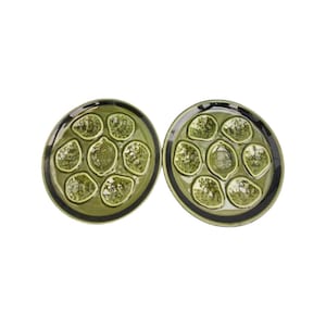 May include: Two green ceramic plates with a black rim. Each plate has seven indented sections that resemble a lemon or lime.
