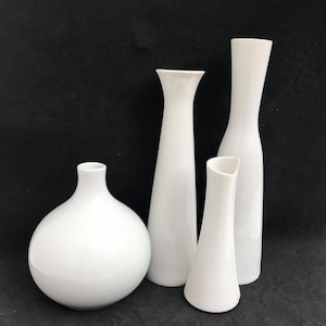 May include: Four white ceramic vases of different shapes and sizes. The vases are arranged on a black background.