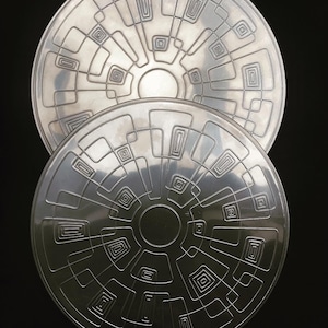 May include: Two silver circular metal trays with a geometric design of concentric squares and rectangles.
