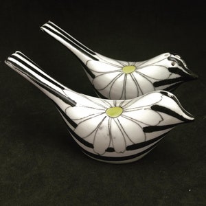 Può includere: Un paio di saliere e pepiere in ceramica a forma di uccelli con strisce bianche e nere e una margherita bianca con un centro giallo su ciascuna.