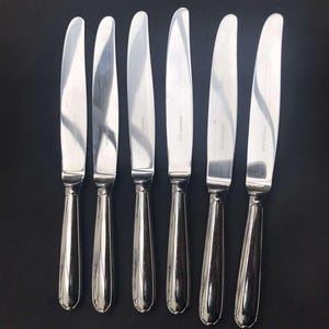 May include: Six silver dinner knives with a polished finish and rounded handles.