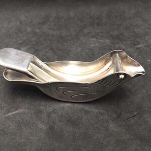 May include: A silver bird-shaped citrus juicer with a hinged top and a small hole in the beak for pouring.