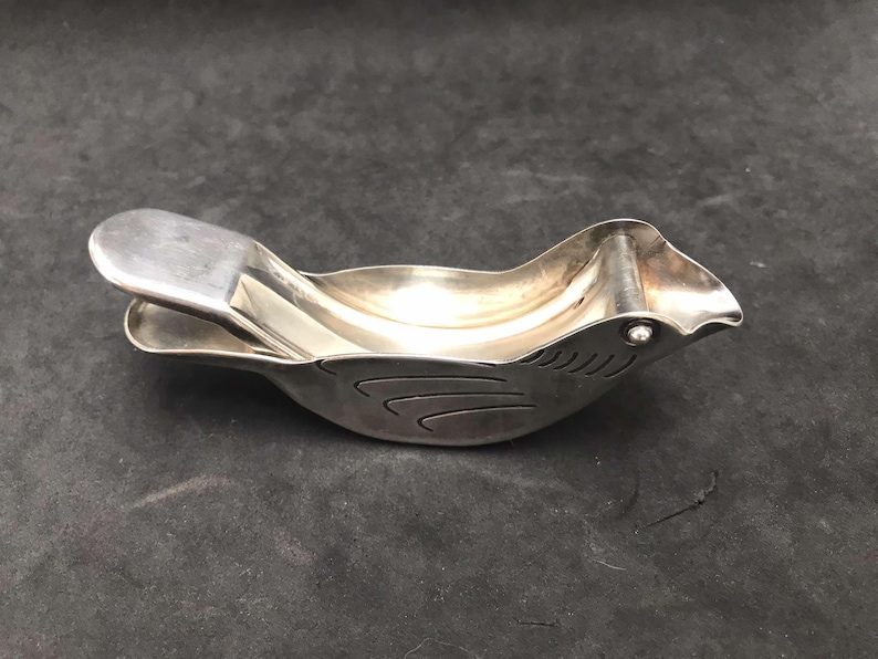 May include: A silver bird-shaped citrus juicer with a hinged top and a small hole in the beak for pouring.