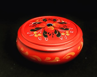 May include: A red wooden box with a painted floral design. The lid has a black and gold floral pattern with a red center. The box is decorated with gold accents.