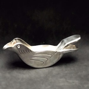 May include: A silver bird-shaped citrus juicer with a hinged beak. The juicer has a smooth, metallic finish and a detailed bird design.
