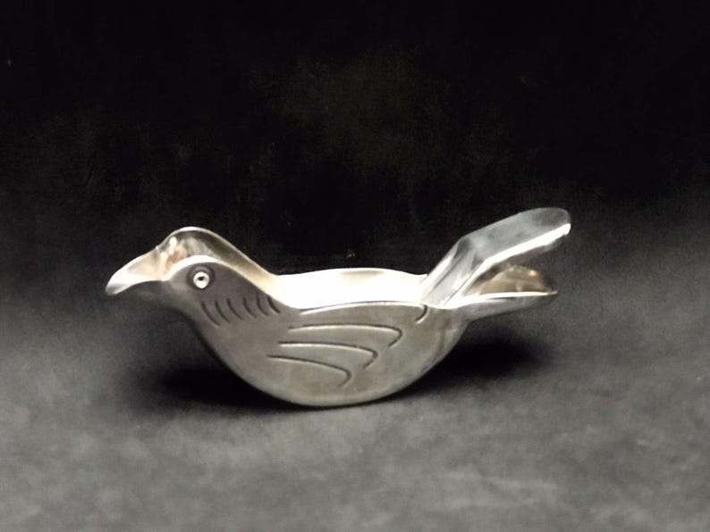 May include: A silver bird-shaped citrus juicer with a hinged beak. The juicer has a smooth, metallic finish and a detailed bird design.