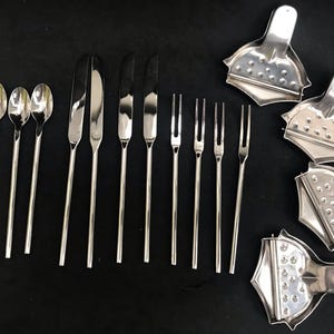 May include: A selection of stainless steel cutlery and citrus juicers. The set includes long-handled spoons, butter knives, forks, and several juicers. The items are arranged on a dark surface, highlighting their polished, reflective surfaces.
