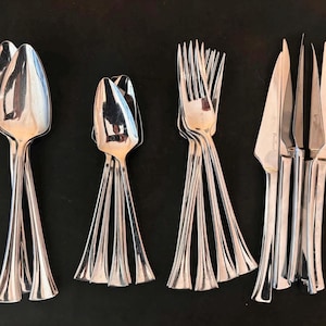 May include: A set of polished silverware, including spoons, forks, and knives, arranged on a dark surface. The silverware has a unique design with a flared base and a tulip-shaped spoon bowl. The knives have a serrated edge.
