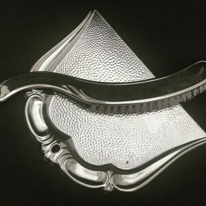 Peut inclure: Un balai à poussière en argent avec une brosse fixée au manche. Le balai à poussière a une surface texturée et un design décoratif.